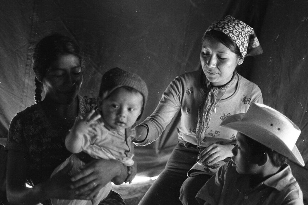 A baby receives attention from grown ups in side a tent.