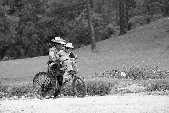 A boy and a man on a bicycle. B/W.