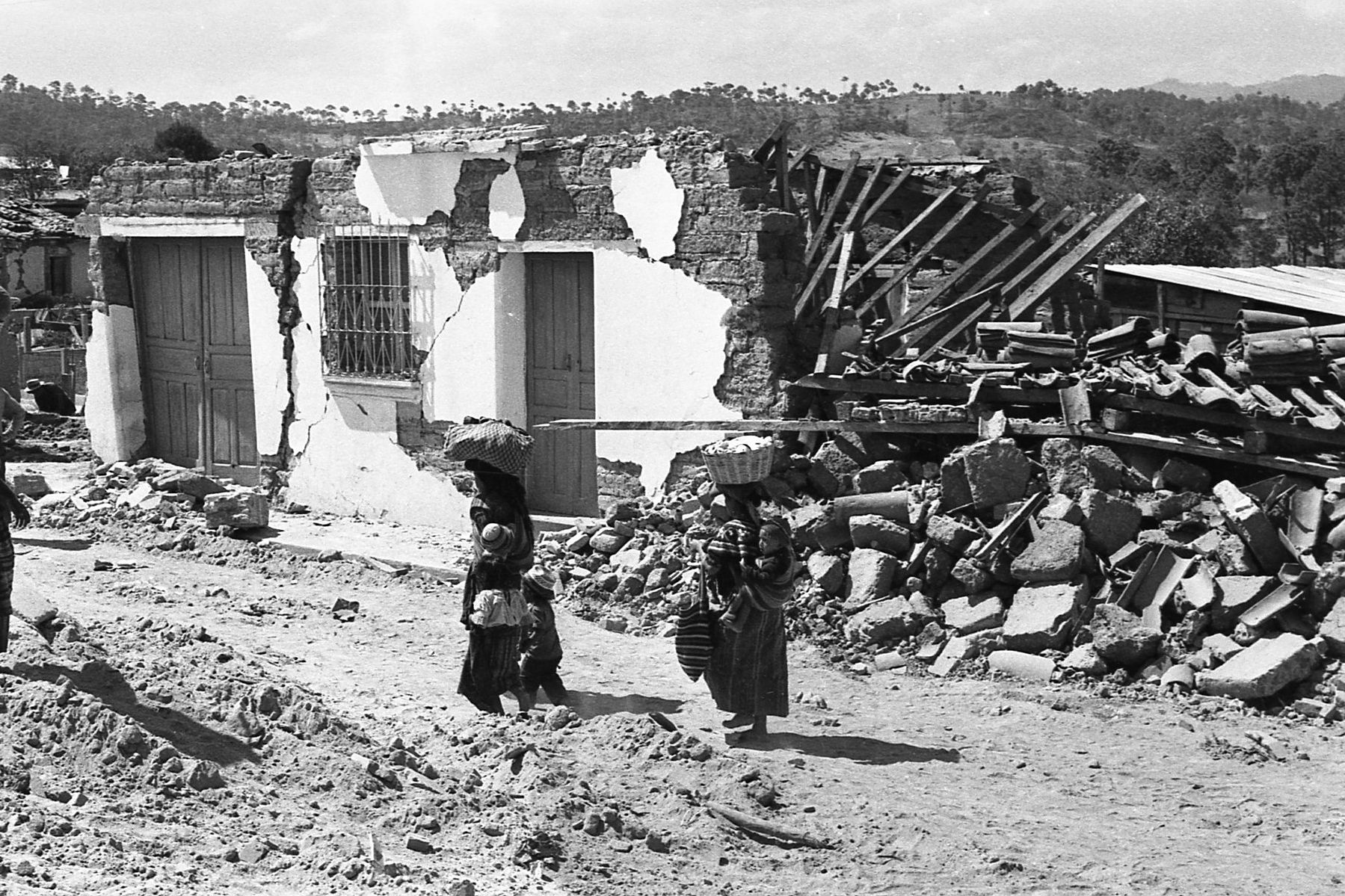 B/W photo of two women walking passed collapsed buildings after the eartquake.