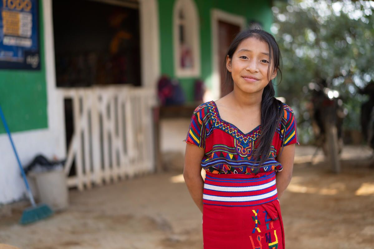 A girl in colourful clothes standing in front of her home.