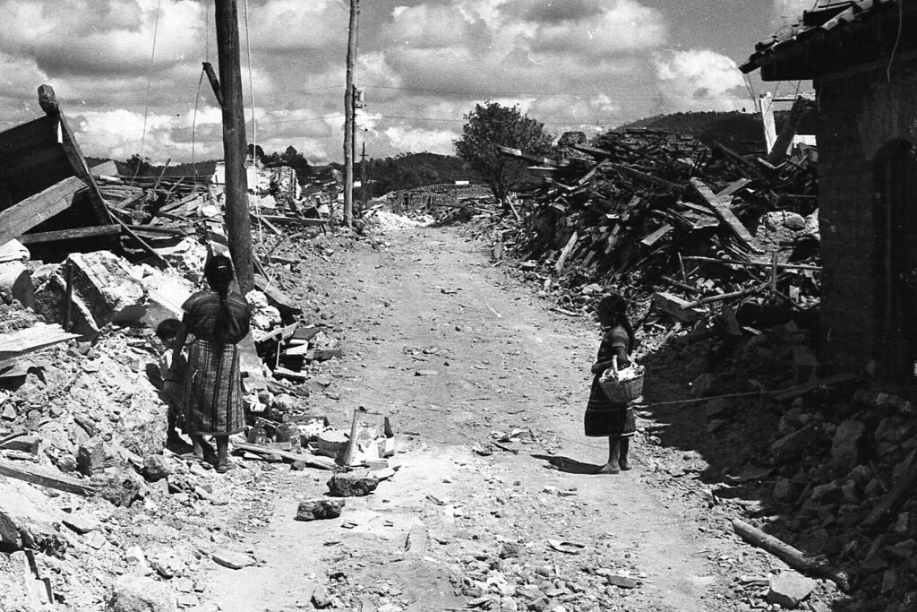Black and white photo of road in village completely destructed by earthquake.