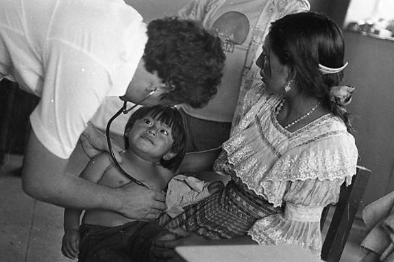 B/W photo of health personal treating a child with a stethoscope.